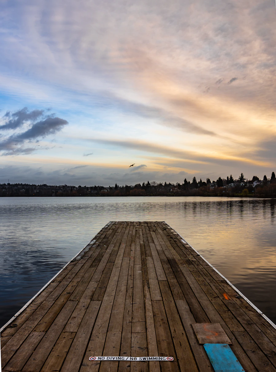 A wooden swimming dock reaching out over the calm water of Green Lake in Seattle at golden hour