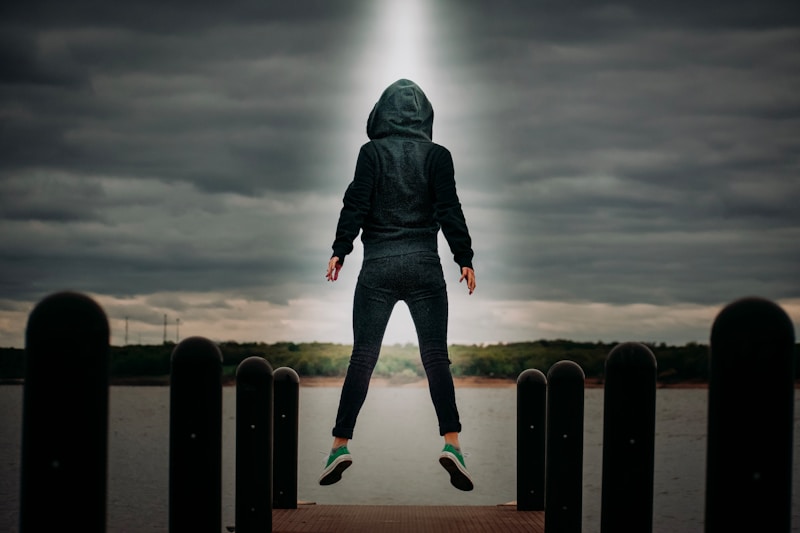 man in black hoodie and blue denim jeans standing on black metal fence under gray clouds