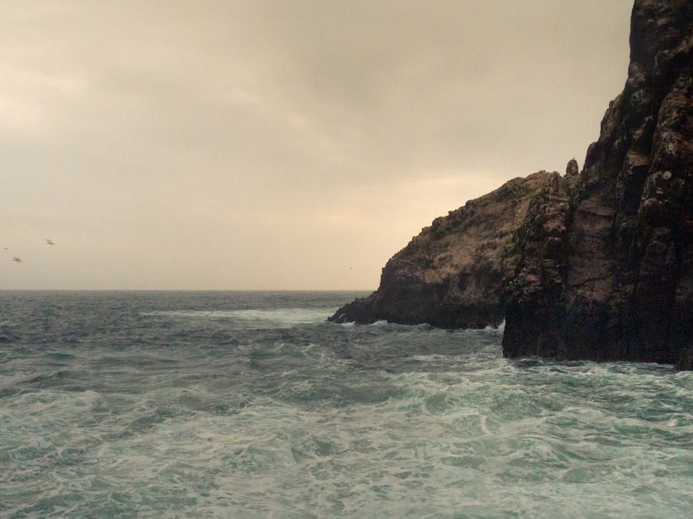 brown rock formation on sea under white clouds during daytime