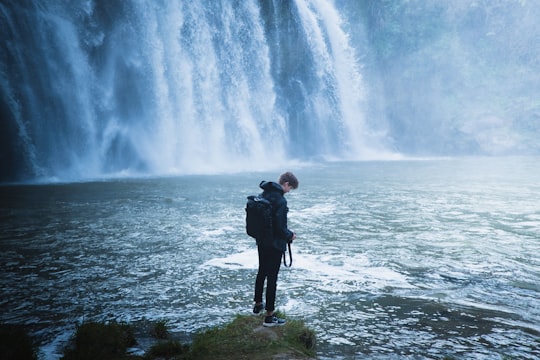 man in black jacket standing on green grass near water falls during daytime in Waihi Falls Road New Zealand