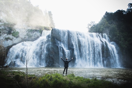 man standing on rock near waterfalls during daytime in Waihi Falls Road New Zealand