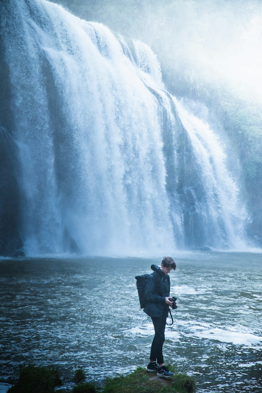 man in black jacket standing near waterfalls during daytime