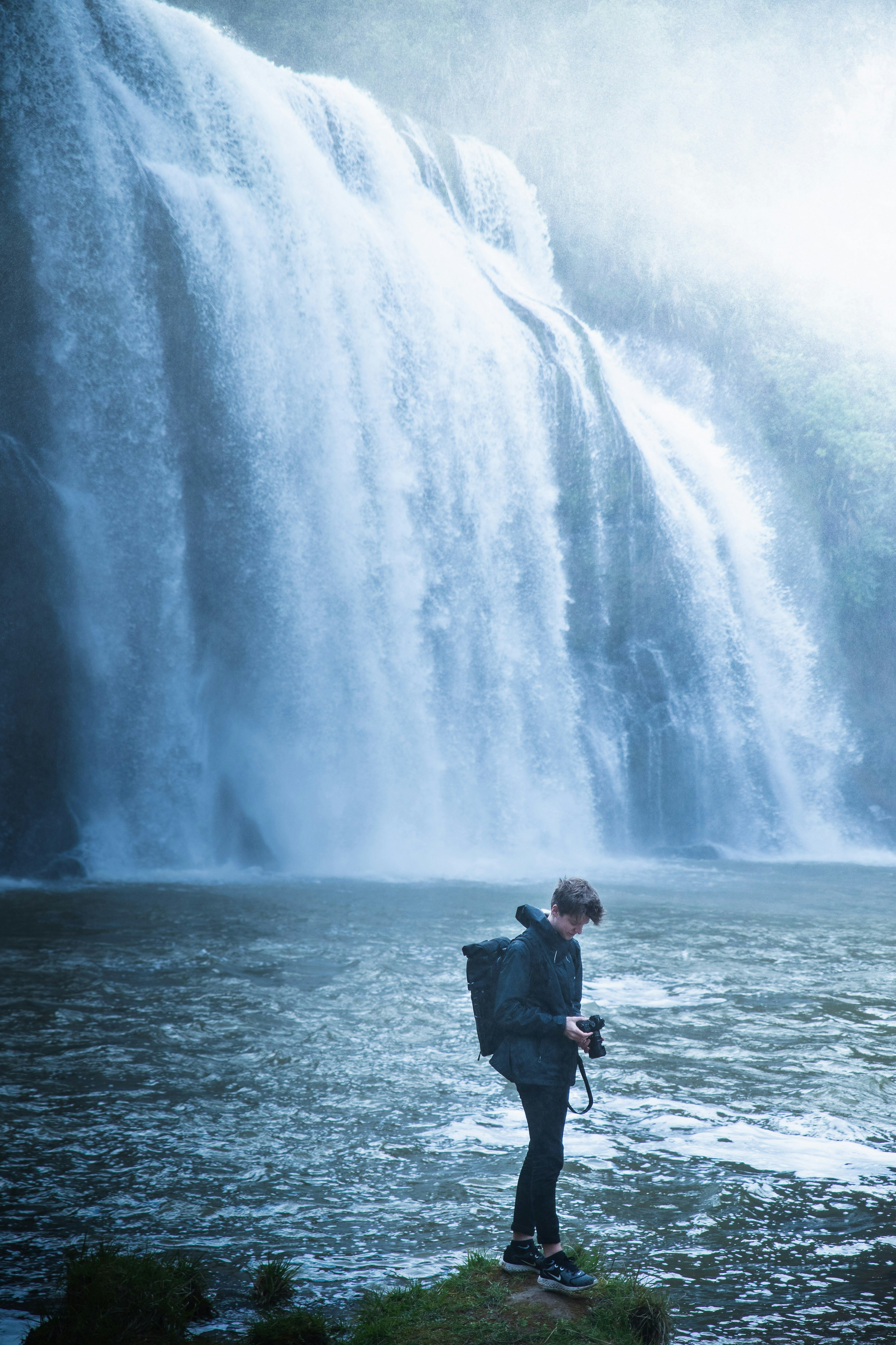 man in black jacket standing near waterfalls during daytime