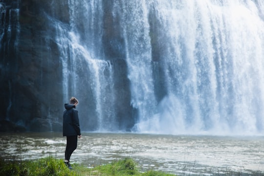 man in black jacket standing in front of waterfalls during daytime in Waihi Falls Road New Zealand