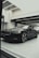 A sleek, black luxury car is parked indoors under modern lighting. The reflective surface of the car highlights its polished finish and sharp design lines. The setting appears to be a sophisticated showroom with ceiling lights casting a soft glow.