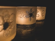 Three decorative candle holders with floral patterns and swirling designs sit in a dimly lit environment. The glow of the candlelight creates a warm and intimate ambiance.
