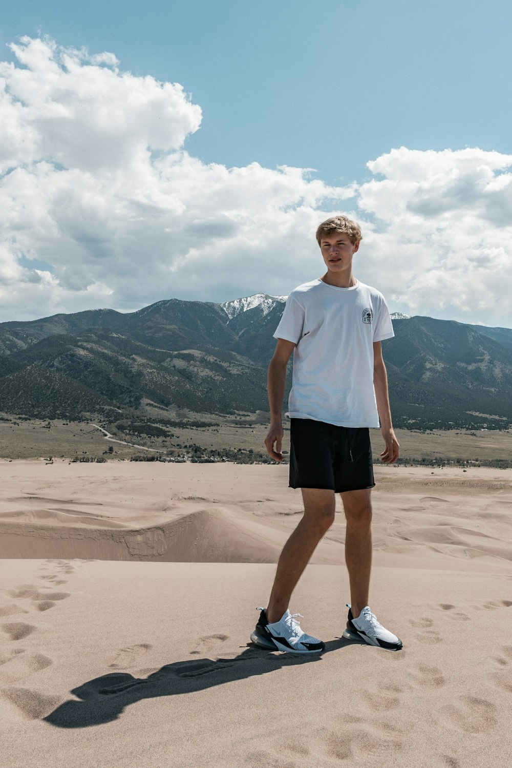 man in white crew neck t-shirt and black shorts standing on brown sand during daytime