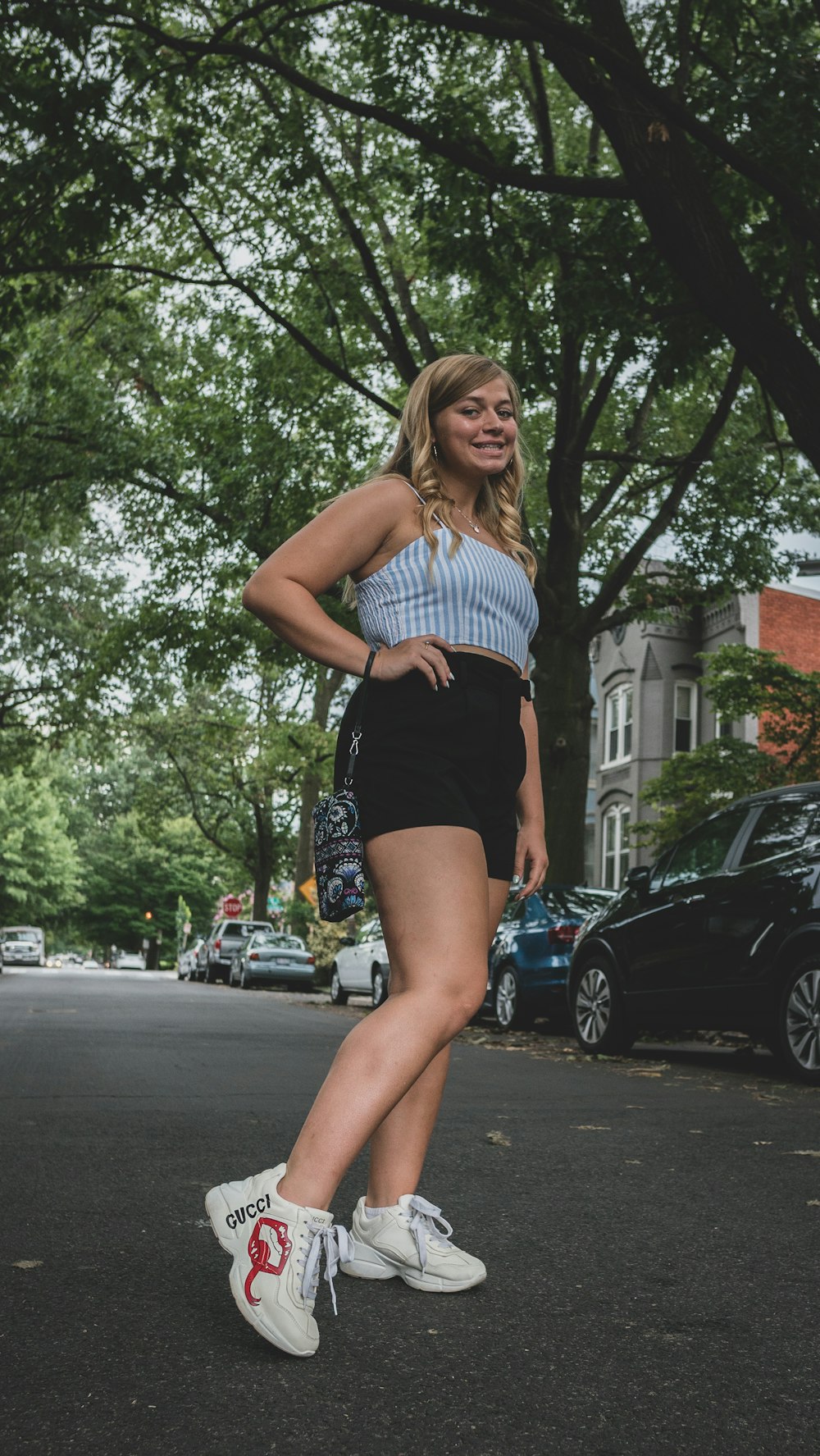 woman in white and blue stripe tank top and black shorts standing on road during daytime