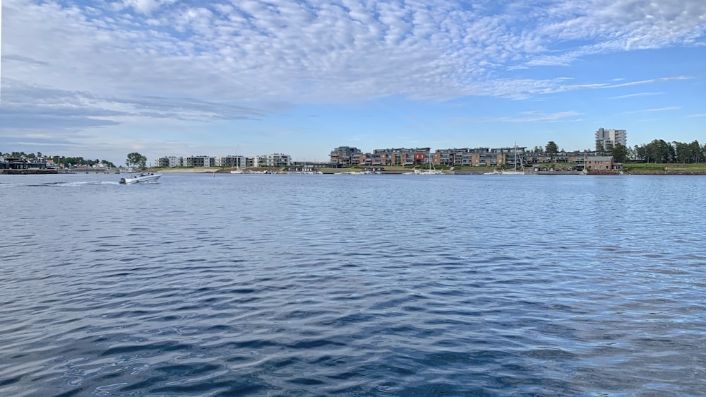 body of water near city buildings under blue and white sunny cloudy sky during daytime