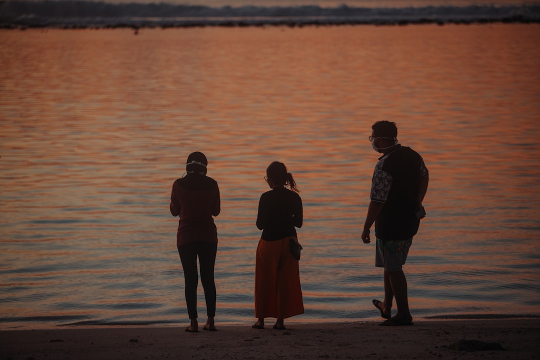 silhouette of 3 men standing on seashore during sunset