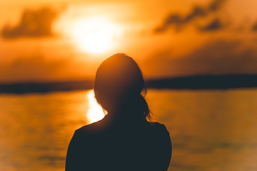 silhouette of woman standing near body of water during sunset