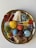 A decorative platter containing an assortment of handcrafted items resembling yarn balls, a white draped cloth, buttons, and a spherical blue object with colorful pins. These items are creatively arranged on an ornate golden dish.