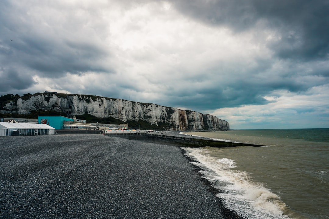 gray rocky mountain beside body of water under cloudy sky during daytime