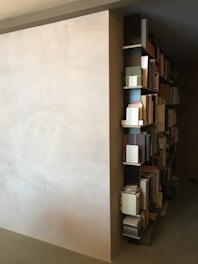 A sleek minimalist wrought iron bookshelf holding a neat row of books against a white wall.