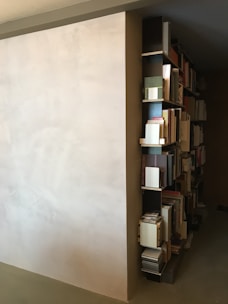 A sleek minimalist wrought iron bookshelf holding a neat row of books against a white wall.