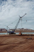 Wide shot of a crane lifting structural elements at a large infrastructure project near rugged terrain.