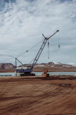 Wide shot of a crane lifting structural elements at a large infrastructure project near rugged terrain.