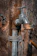 A metal water tap is attached to a rusty pipe, with a rope tied around the pipe. The background consists of a textured tree bark, providing a rustic and natural setting.