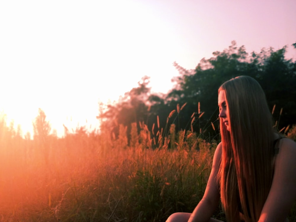 woman in black tank top sitting on green grass field during sunset