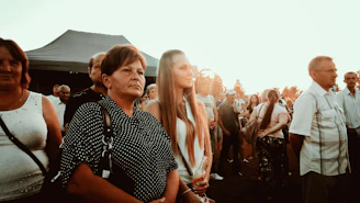 A diverse group of people united in worship and prayer outdoors at sunset.