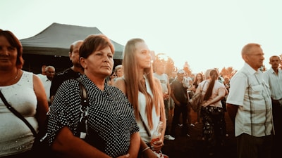 A diverse group of people listening intently during an outdoor speech event at sunset.
