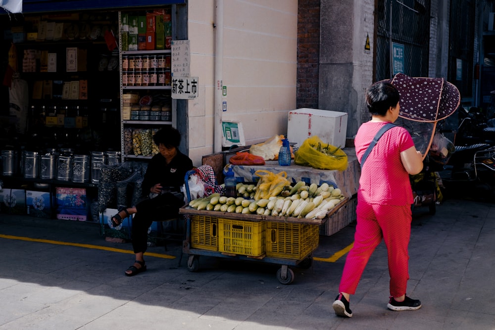 a woman in a pink outfit walking past a fruit stand