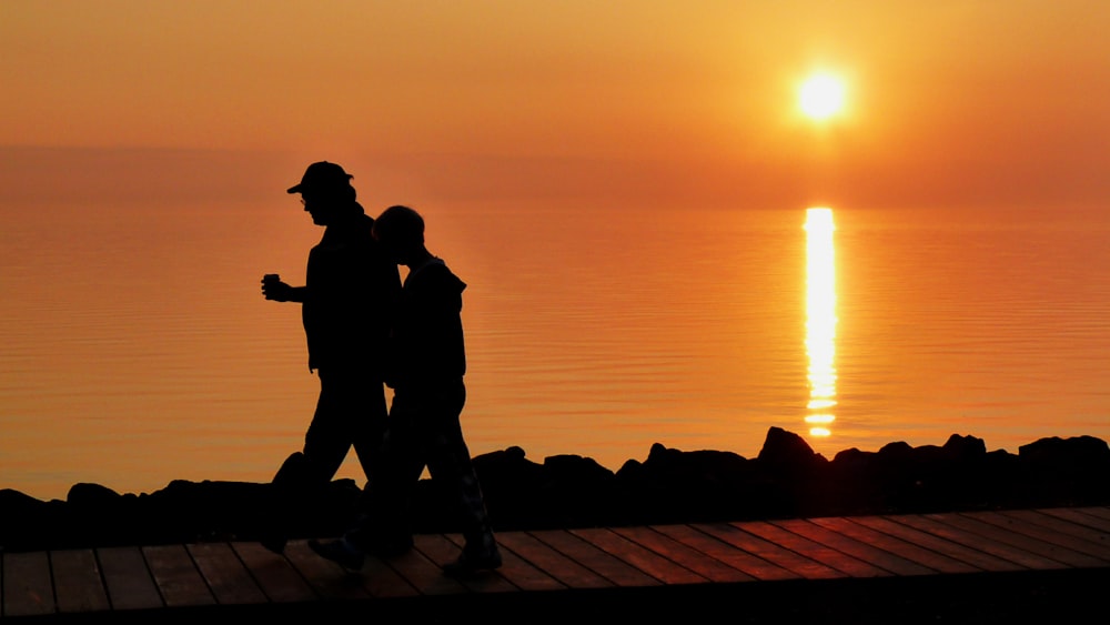 silhouette of 2 men standing on the beach during sunset