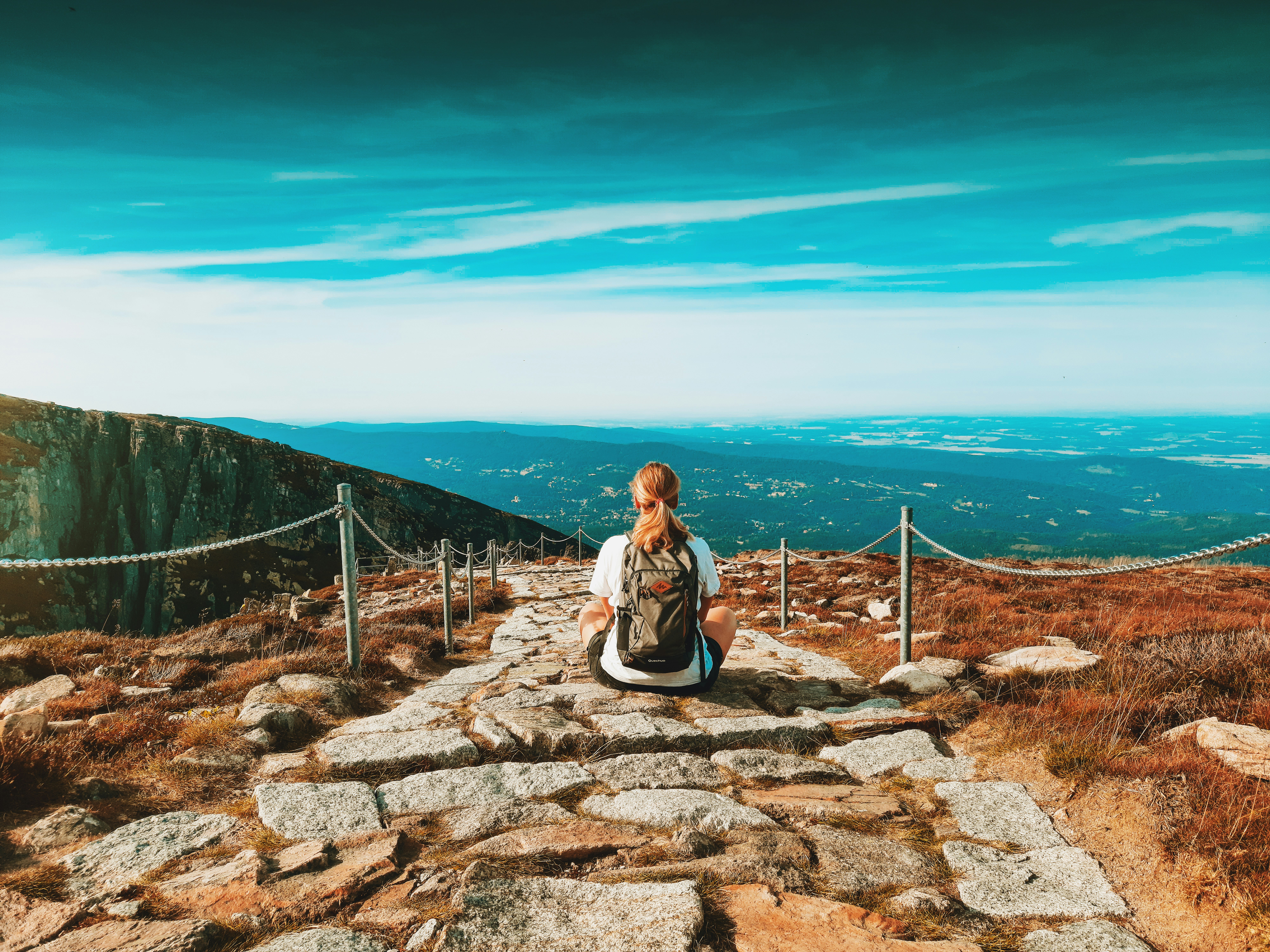 woman in white long sleeve shirt sitting on gray concrete stairs near blue sea under blue