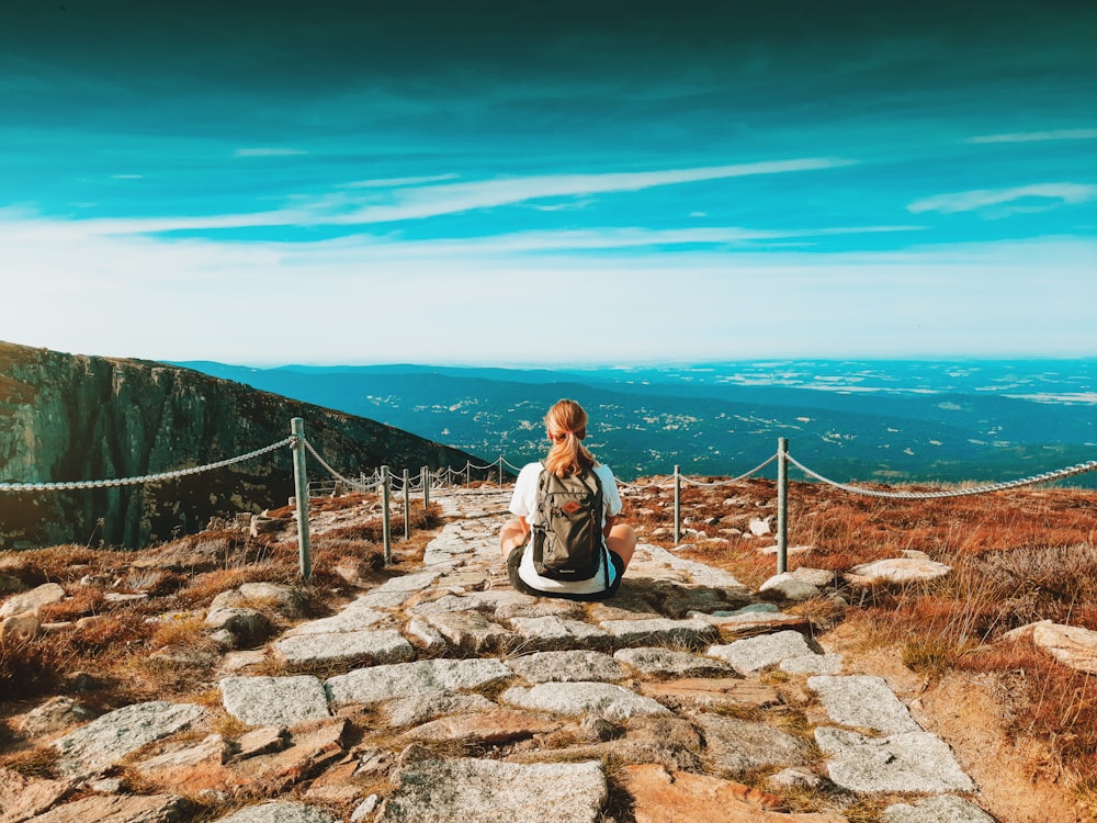 woman in white long sleeve shirt sitting on gray concrete stairs near blue sea under blue