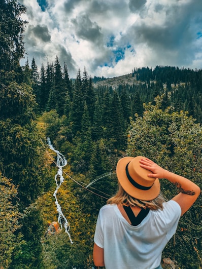 woman in white shirt and brown hat standing on forest during daytime