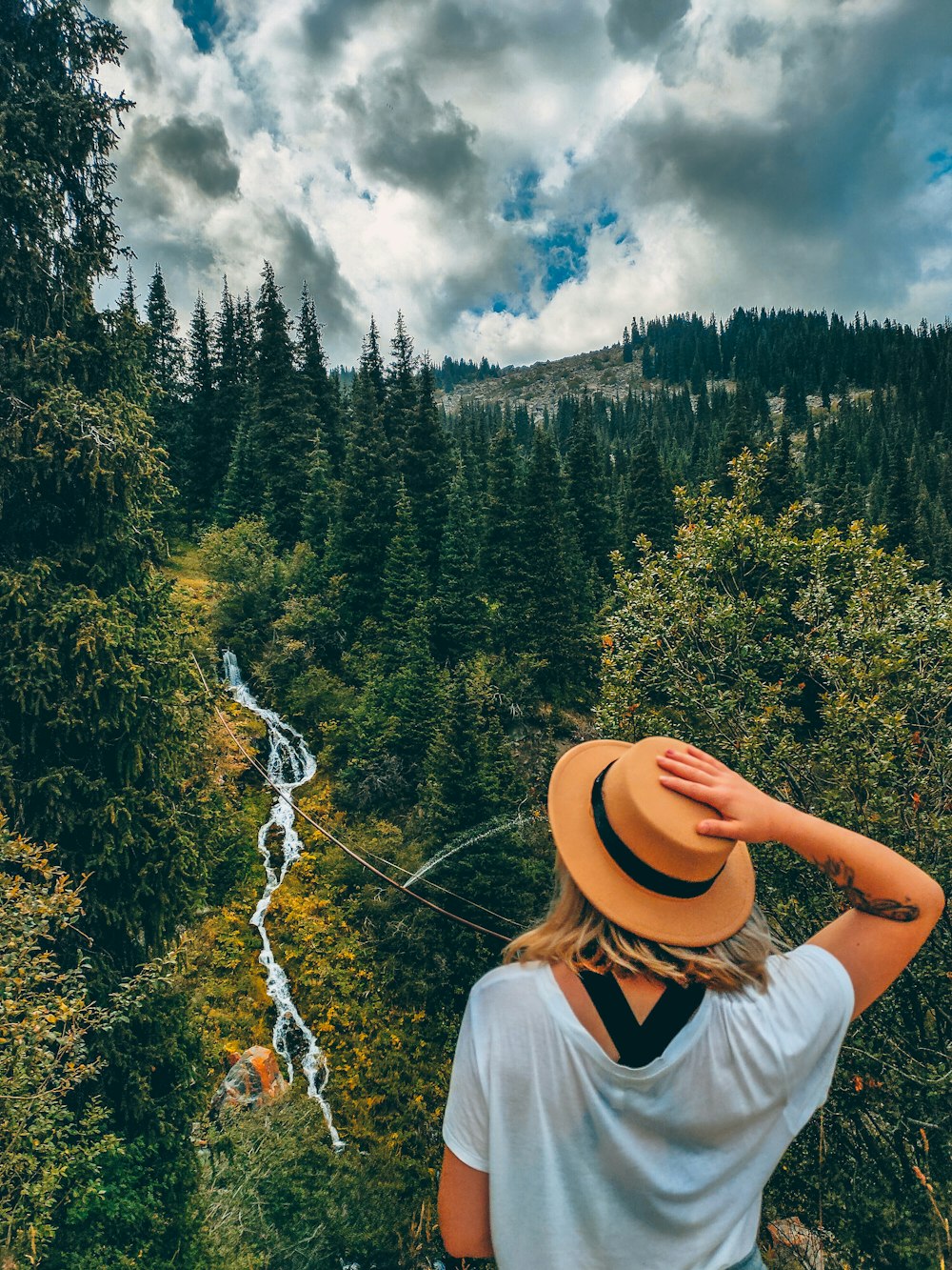 woman in white shirt and brown hat standing on forest during daytime