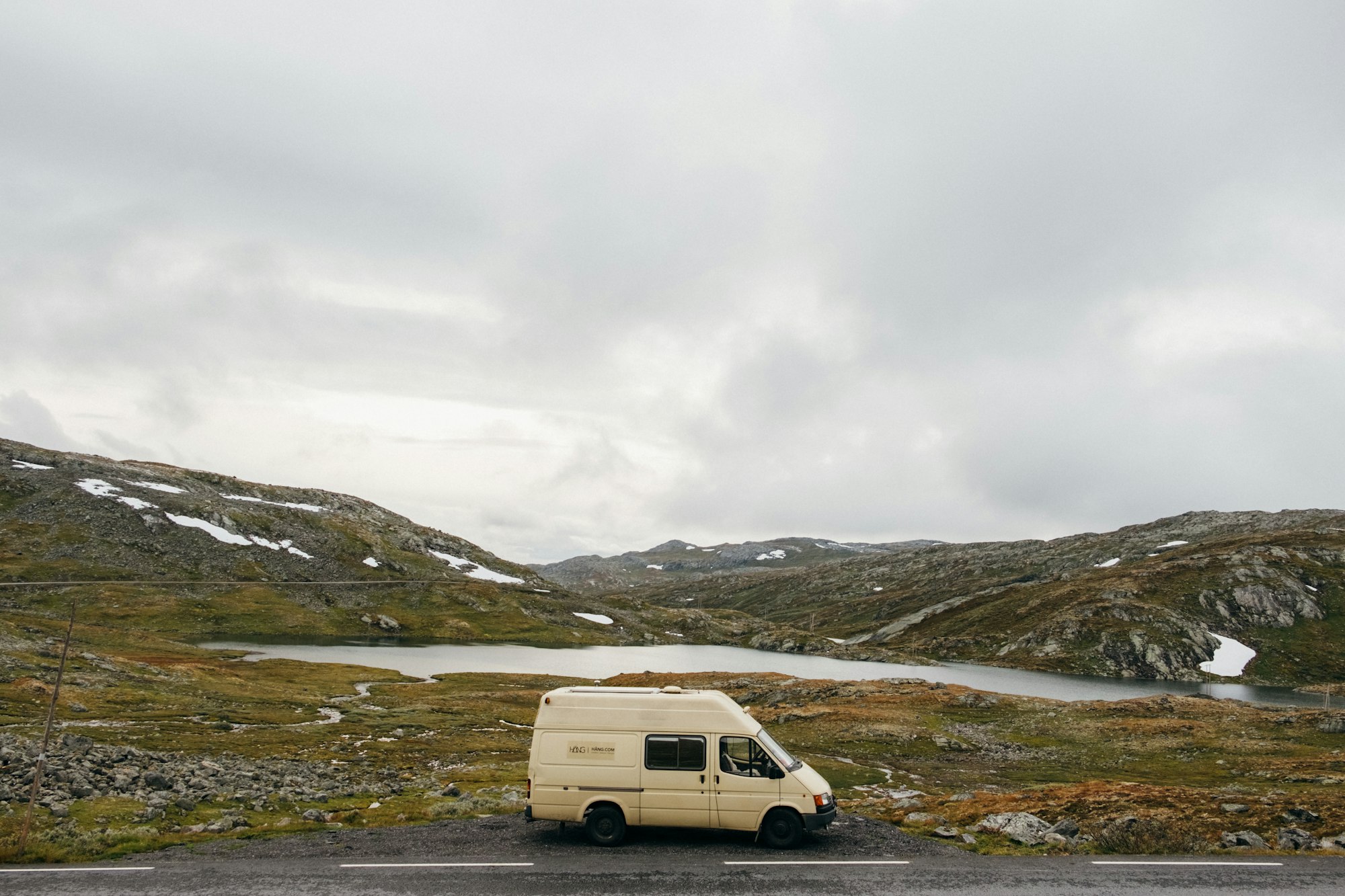 white camper rental van on green grass field under white cloudy sky during daytime