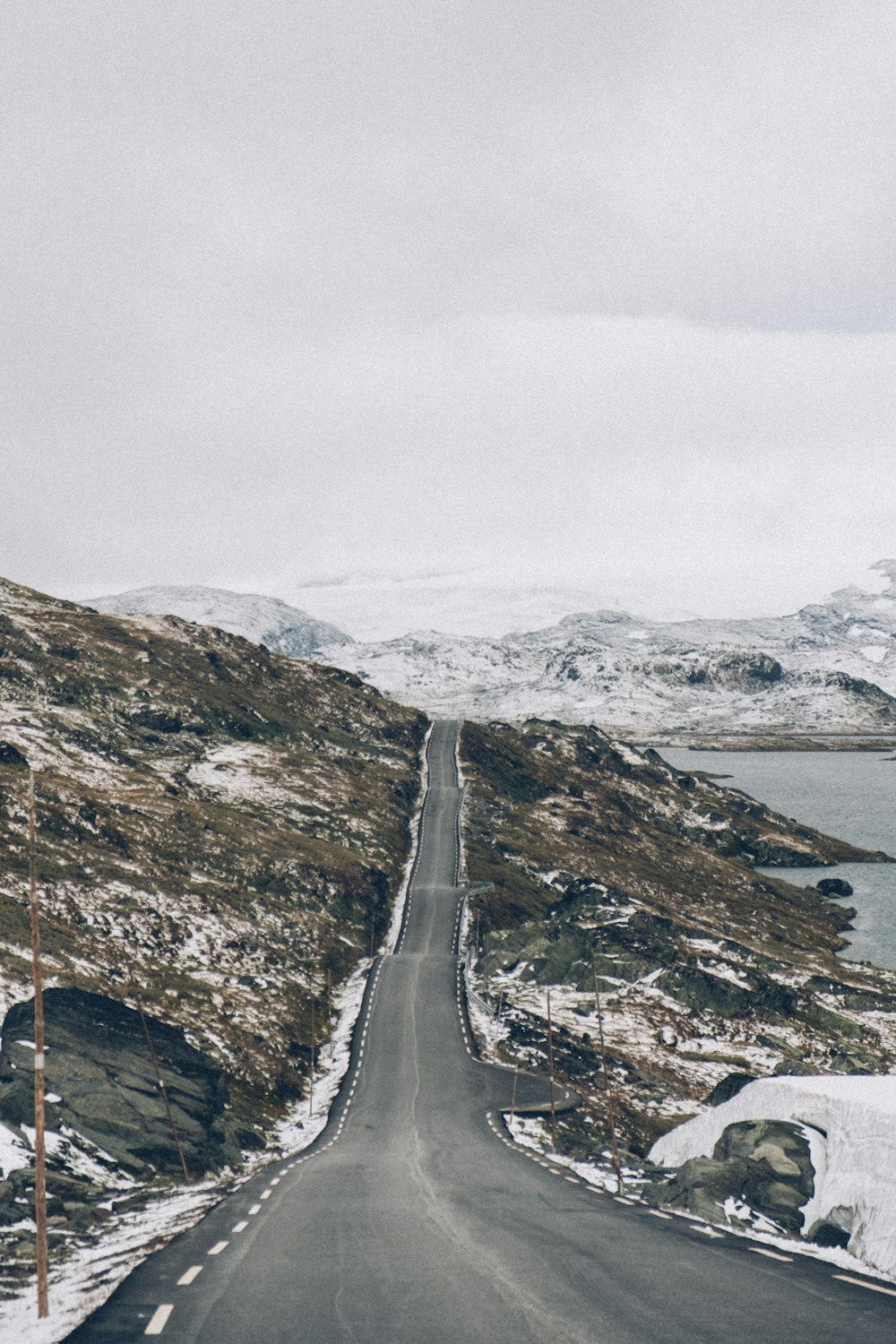 Carretera gris entre montañas marrones y verdes bajo el cielo blanco durante el día