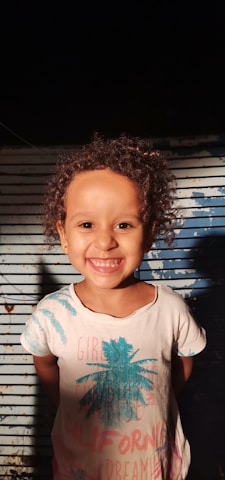 A vibrant display of the Jamaican flag colors with a child wearing the 'Bless the Children' t-shirt, smiling warmly.