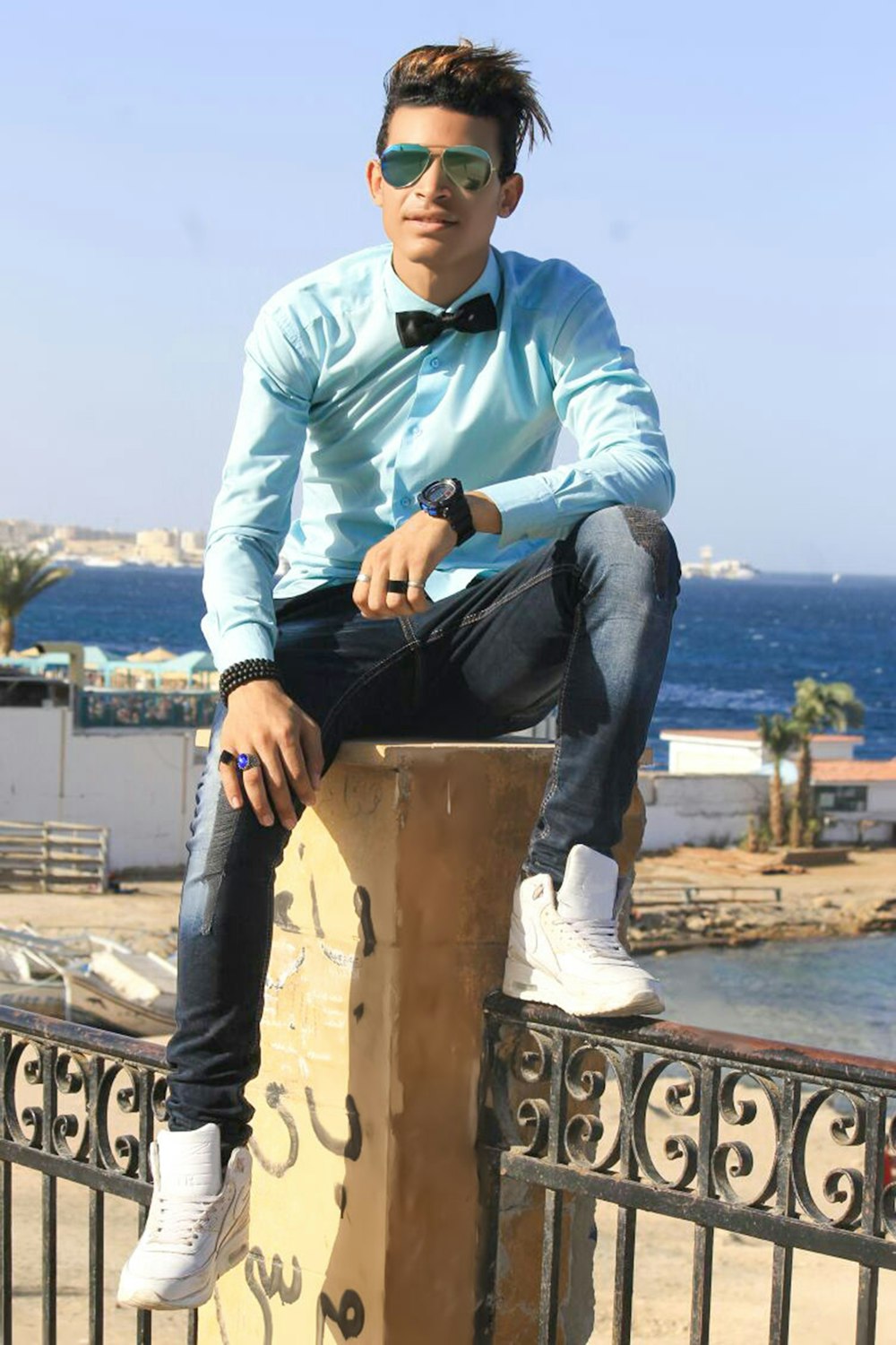 man in white dress shirt and blue denim jeans sitting on brown concrete fence during daytime