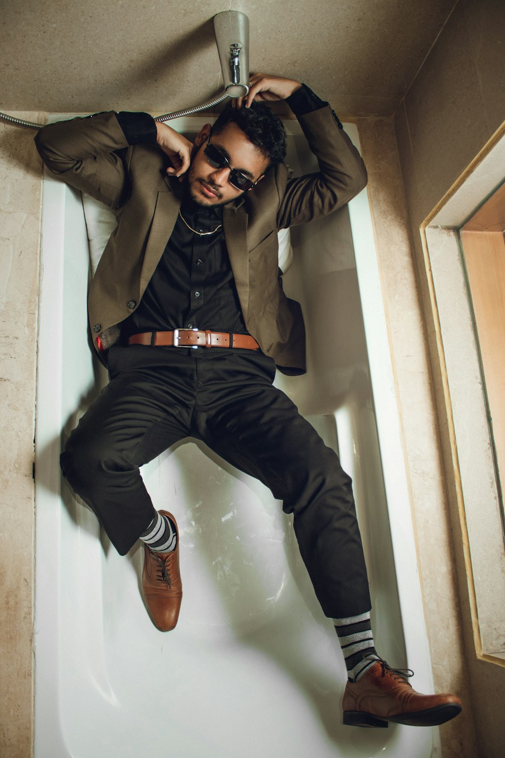 man in brown jacket and blue denim jeans sitting on white ceramic bathtub