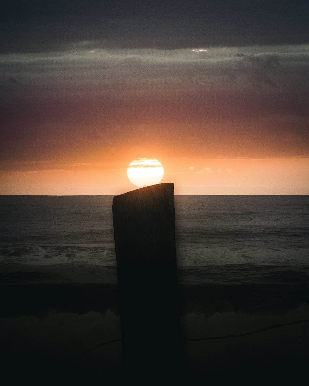 brown wooden post on sea shore during sunset