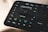 A close-up view of a Loupedeck editing console, featuring various labeled buttons and a central control dial. Buttons include functions such as undo, redo, shift, control, and others related to editing tasks. The interface appears sleek and designed for efficient workflow management.