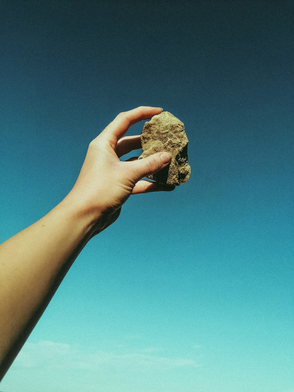 person holding brown rock under blue sky during daytime