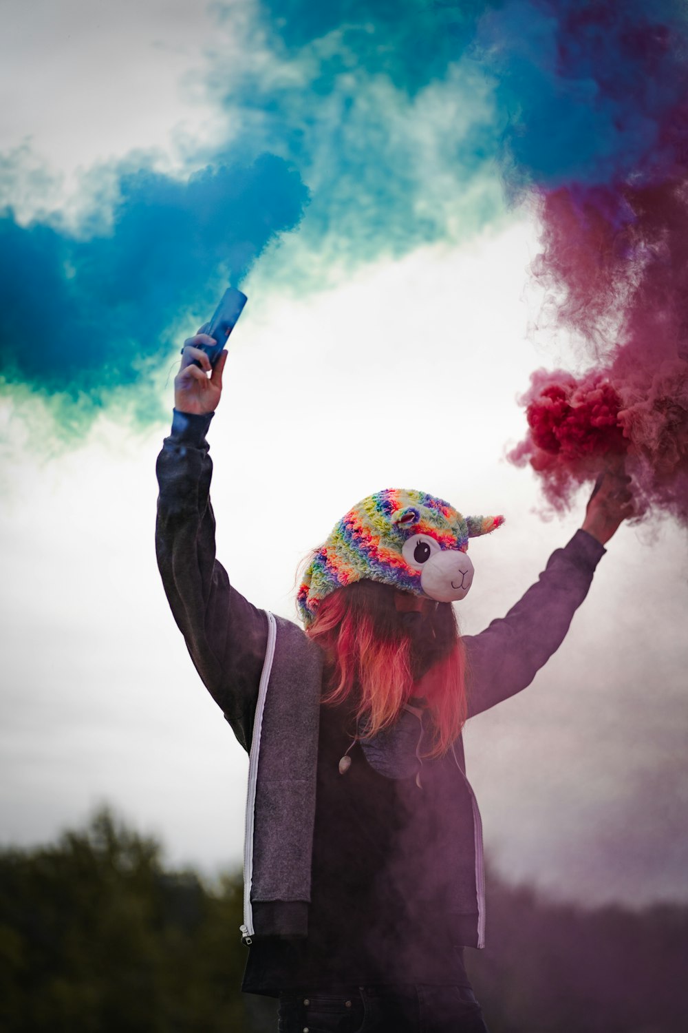 woman in black jacket holding blue and pink smoke