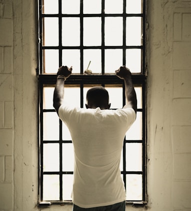 man in white t-shirt standing in front of window