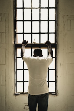 man in white t-shirt standing in front of window