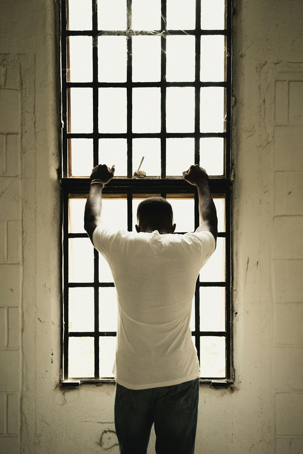 hombre con camiseta blanca de pie frente a la ventana