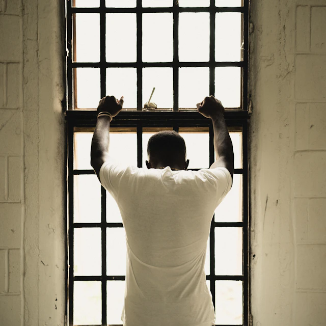 A man in a white T-shirt standing in front of a window