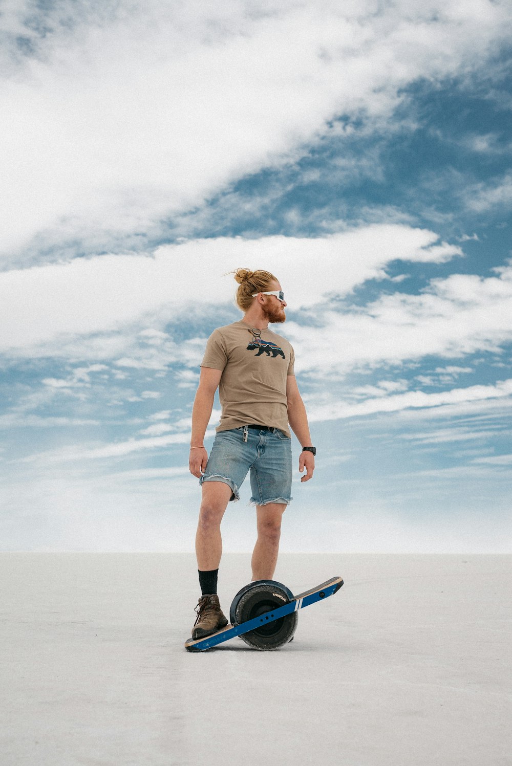 donna in canotta grigia e pantaloncini di jeans blu che cavalca sullo skateboard blu e nero durante