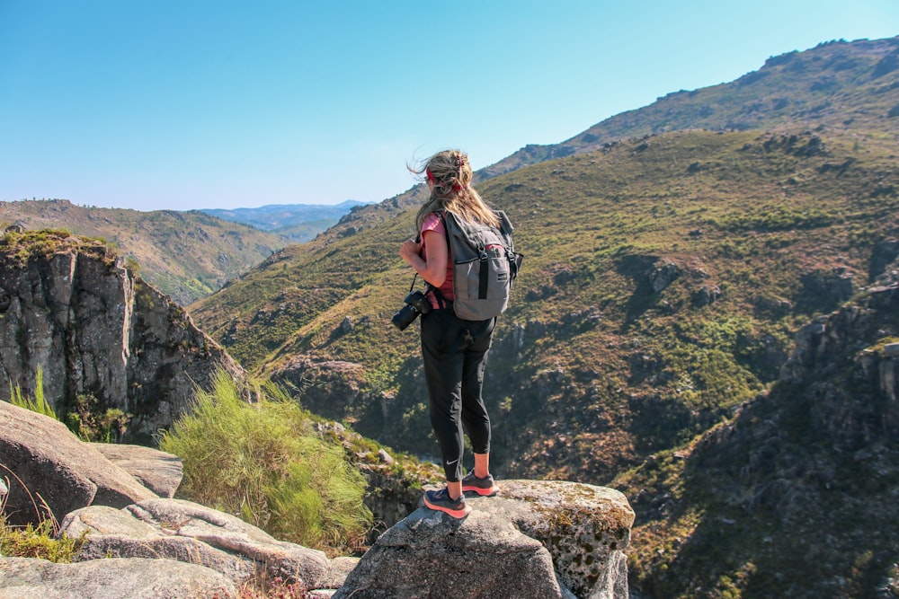 woman in black pants standing on gray rock during daytime