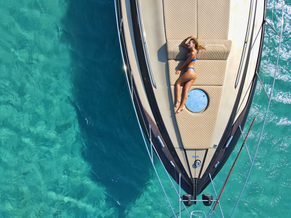 woman in black bikini lying on blue and white boat during daytime