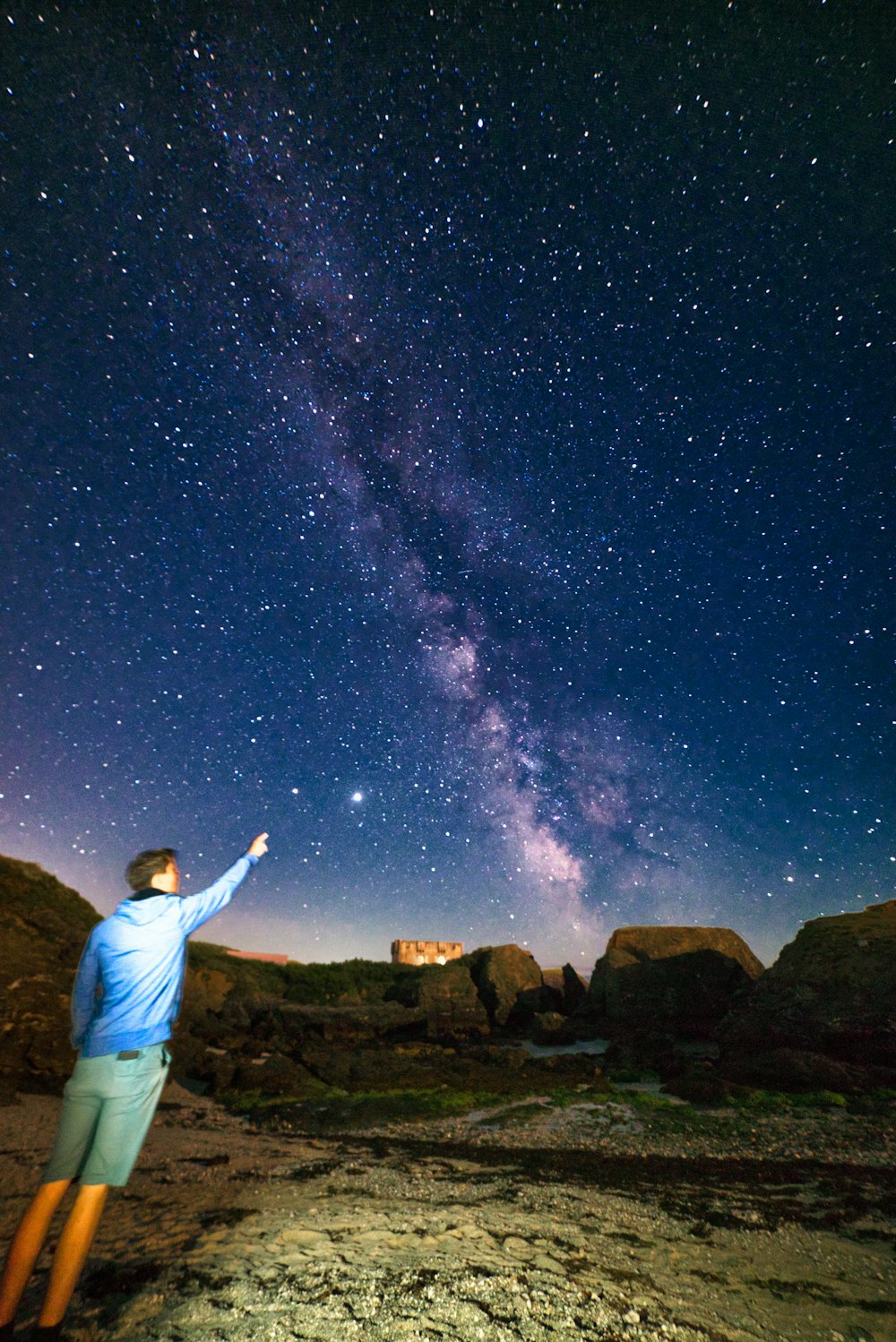 man in white dress shirt standing on brown rock under starry night