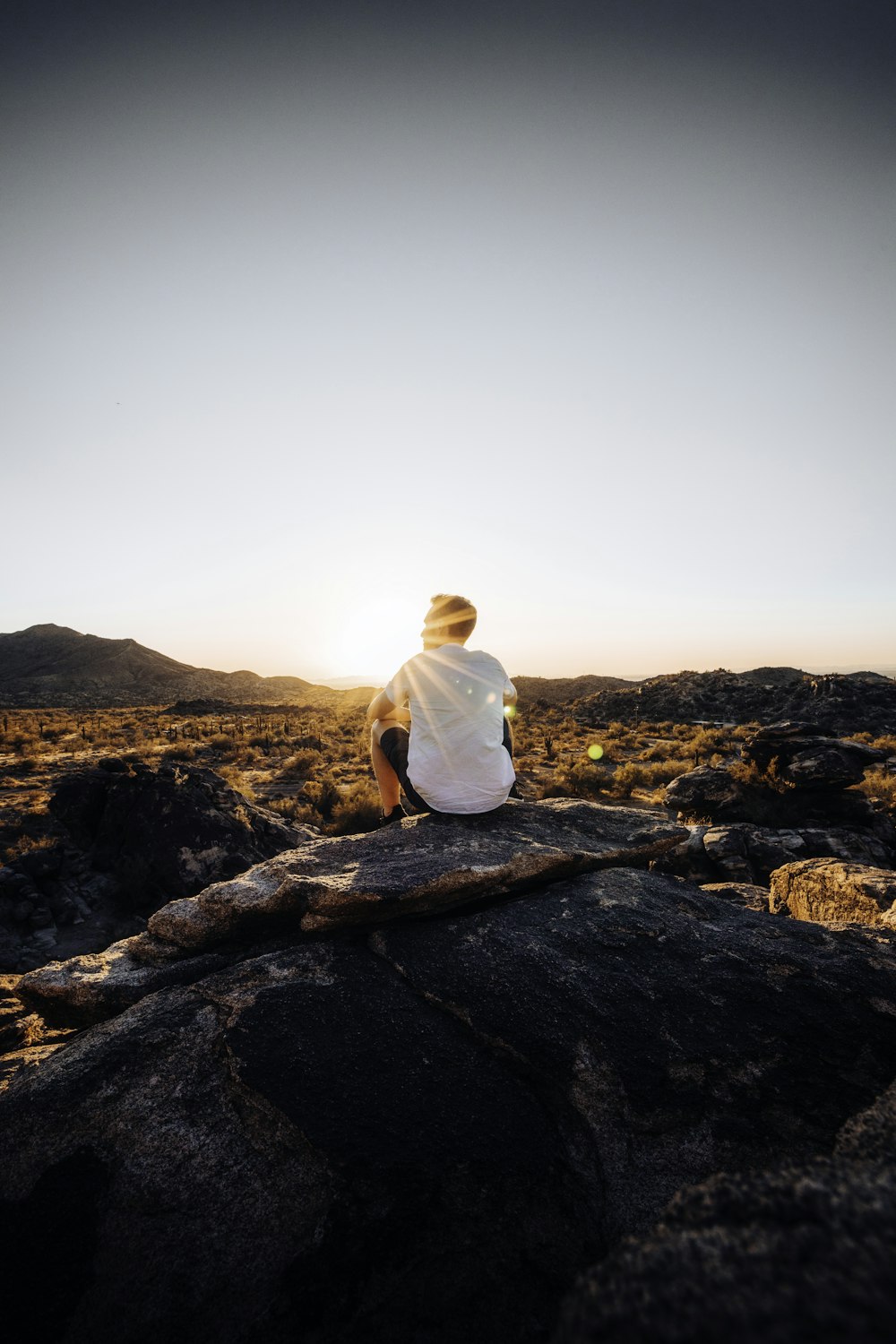 man in white shirt sitting on brown rock during daytime