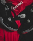 Black athletic shoes are placed alongside red and black sportswear bearing logos from Spalding and The North Face.